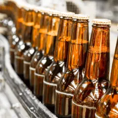 Rząd brązowych butelek piwa na linii produkcyjnej. Czy piwo 0 jest zdrowe? To pytanie nurtuje wielu konsumentów.