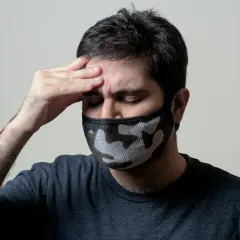 Mężczyzna z maską na twarzy i ręką na czole, cierpiący na objawy przypominające autoimmunologiczne zapalenie mózgu.