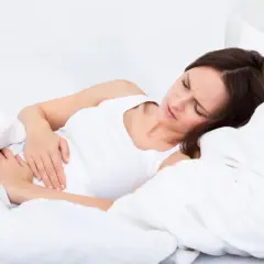 Kobieta w łóżku z ręką na brzuchu, cierpiąca z bólu. Zastanawia się, zatrucie pokarmowe ile trwa.
