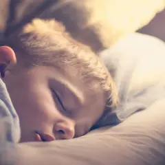 Mały chłopiec śpi spokojnie, otulony kołdrą. Czasem jego oddech staje się głośniejszy, przypominając chrapanie u dziecka.