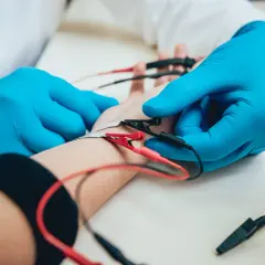 Lekarz w niebieskich rękawiczkach zakłada elektrody na rękę pacjenta. To badanie EMG, które pozwala ocenić funkcję nerwów i mięśni.