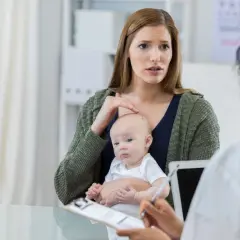 Zmartwiona matka z niemowlęciem rozmawia z lekarzem o objawach, które mogą wskazywać na padaczkę u dzieci.