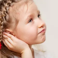 Mała dziewczynka z warkoczem i czerwoną kokardką, dotyka ręką ucha, jakby słuchała czegoś, co szepcze jej guzek za uchem.