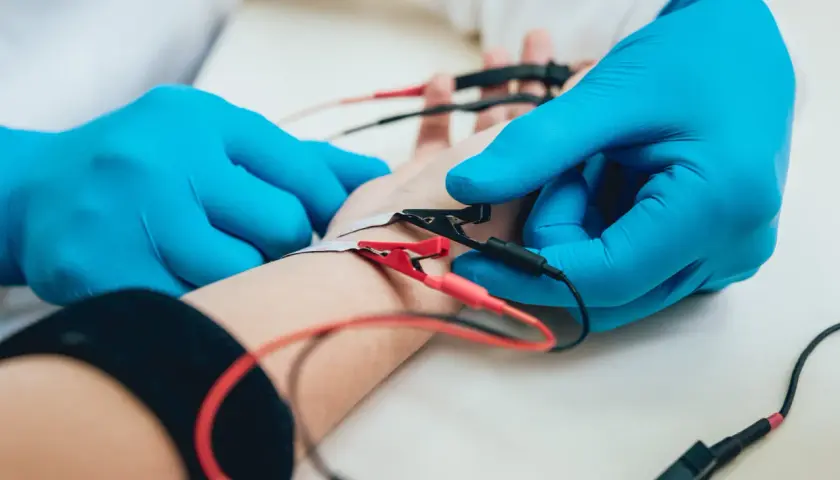Lekarz w niebieskich rękawiczkach zakłada elektrody na rękę pacjenta. To badanie EMG, które pozwala ocenić funkcję nerwów i mięśni.