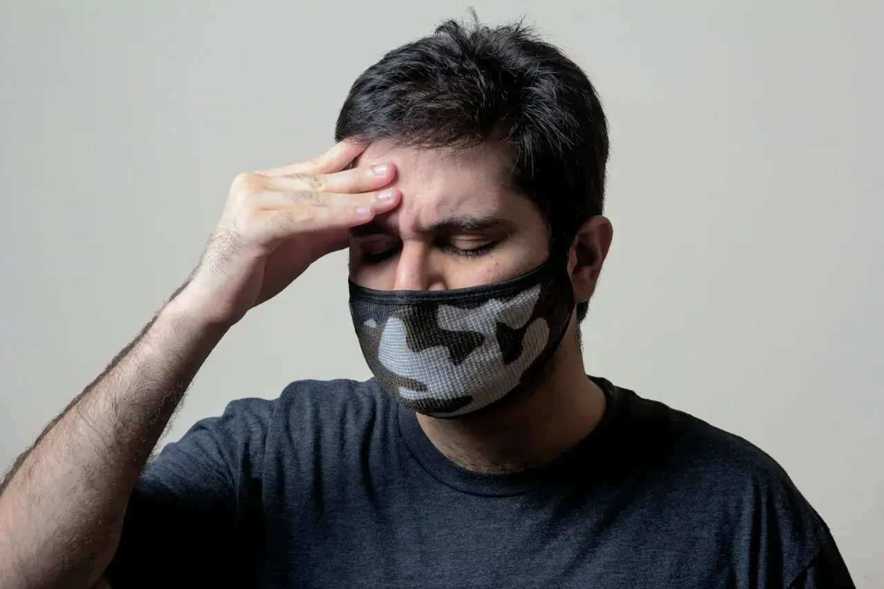 Mężczyzna z maską na twarzy i ręką na czole, cierpiący na objawy przypominające autoimmunologiczne zapalenie mózgu.