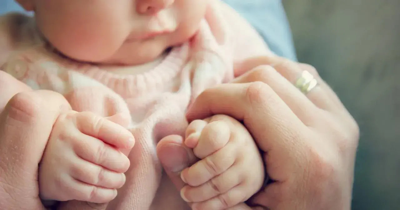 Delikatne dłonie noworodka trzymają palec rodzica. Ulewanie u noworodka to częsty widok, ale te małe rączki symbolizują bezpieczeństwo i miłość.