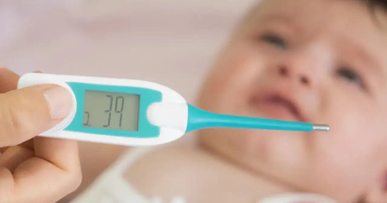Cyfrowy termometr pokazuje 39 stopni. Niemowlę ma gorączkę, co widać po jego zaczerwienionej buzi.