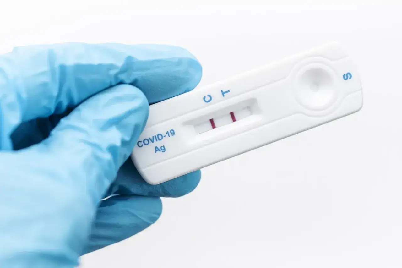 Rękawiczka w niebieskiej rękawiczce trzyma test COVID-19 z dwoma czerwonymi paskami, wskazującymi na pozytywny wynik, co może oznaczać nowy wariant koronawirusa.