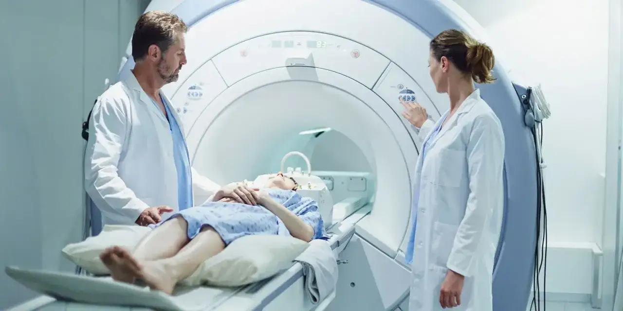 Pacjentka leży w aparacie rezonansu magnetycznego, a lekarze przygotowują badanie. Czy na rezonans trzeba mieć skierowanie? Zwykle tak, aby badanie było refundowane.